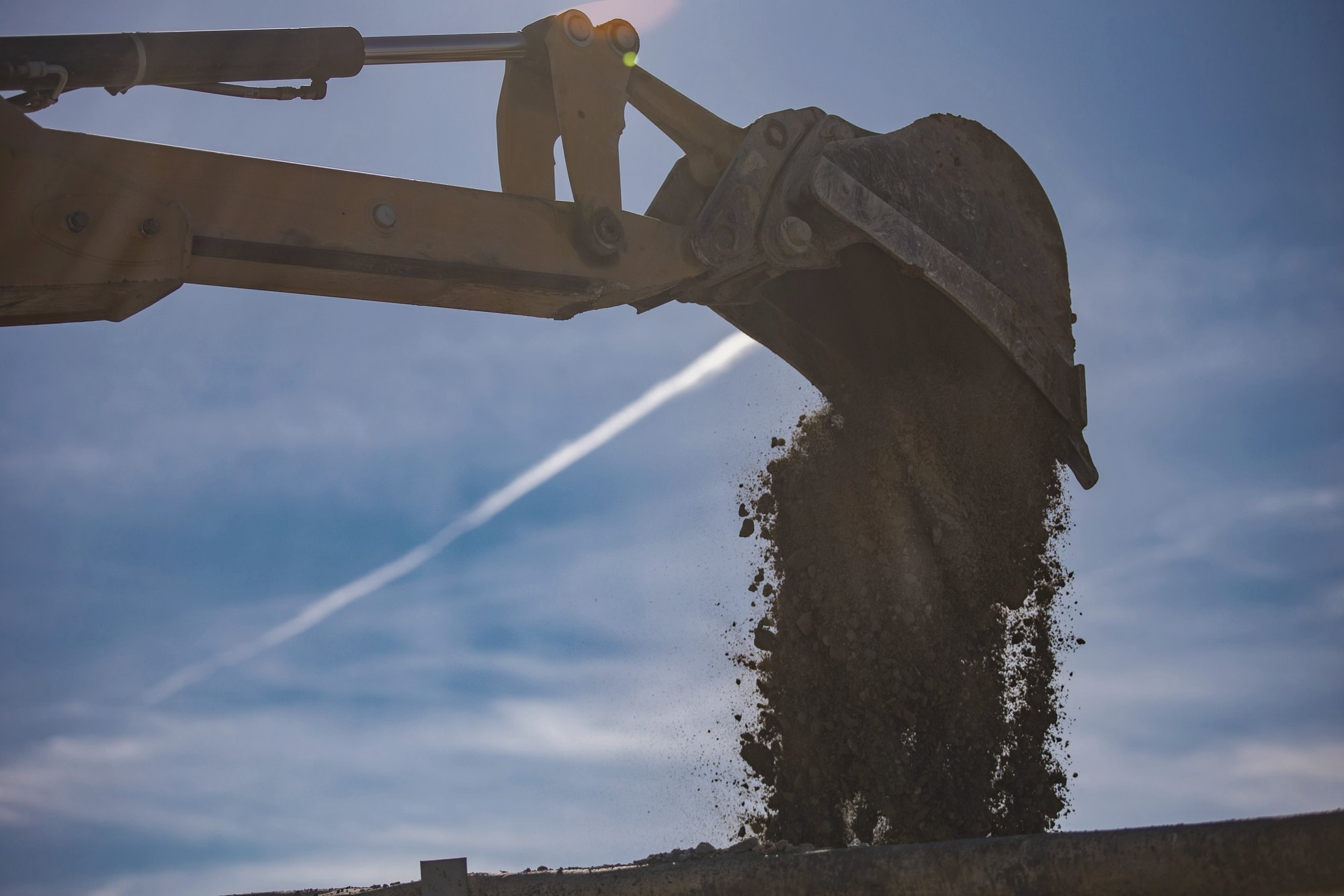 Excavator bucket releasing soil against a clear sky