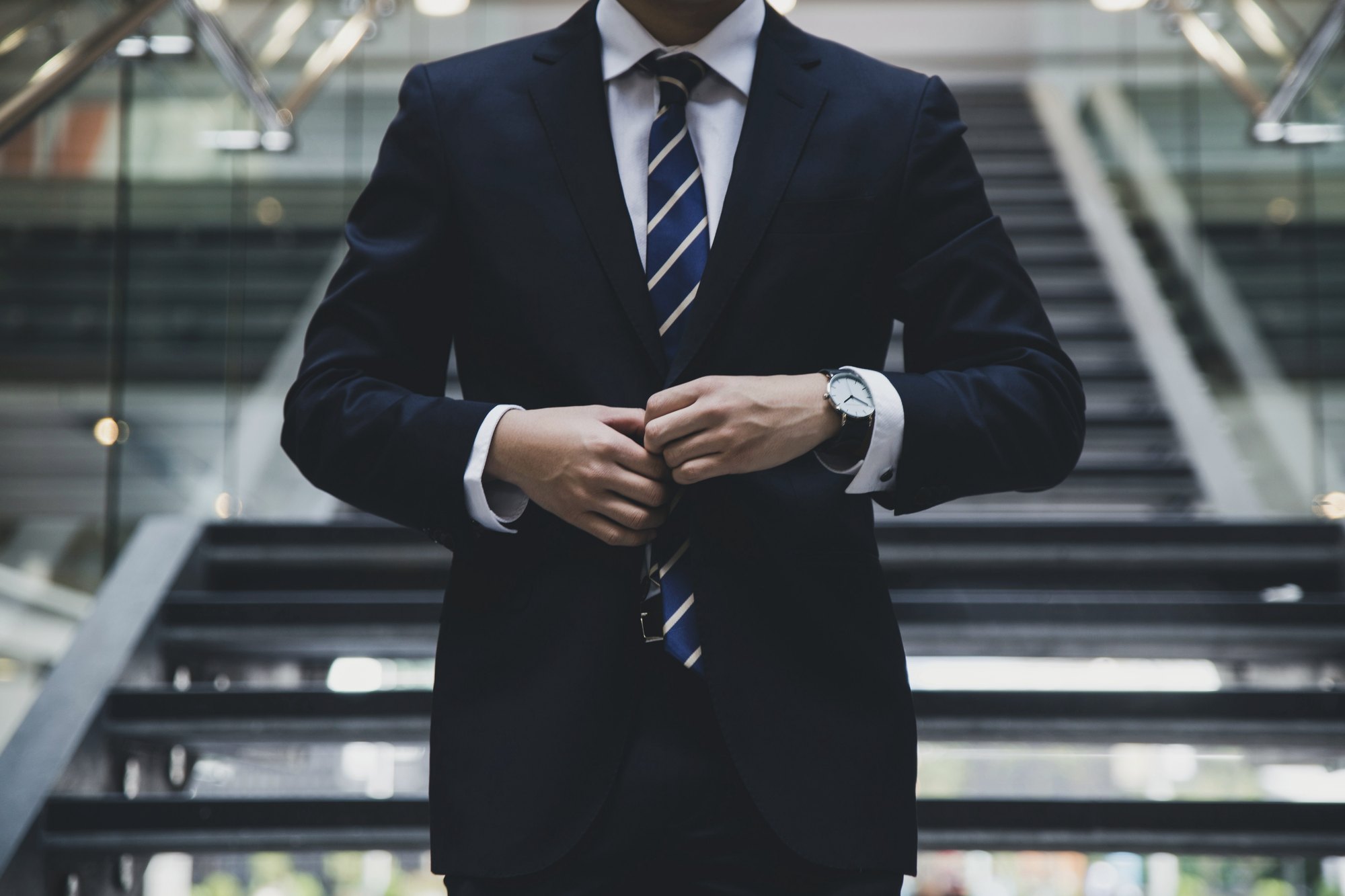 Business owner in a navy suit buttoning his jacket on a staircase